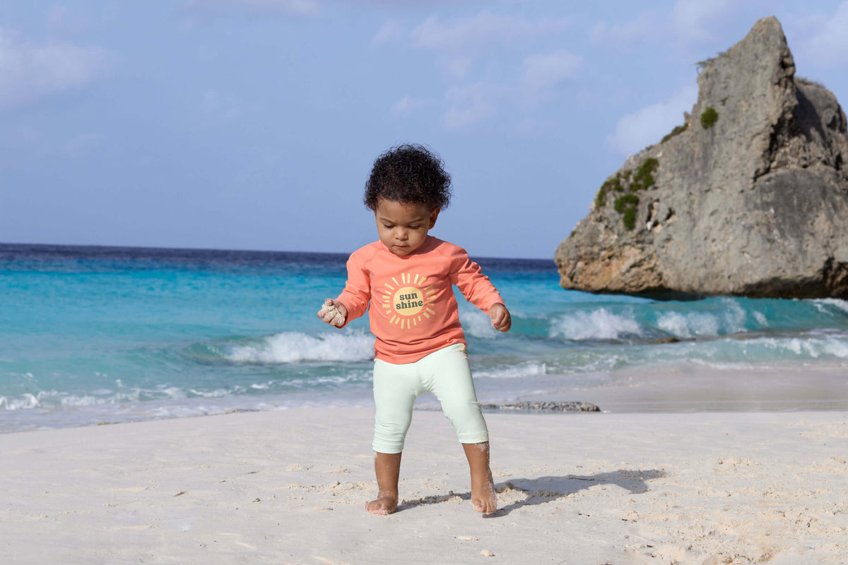 Kind trägt LÄSSIG UV-Shirt in Koralle beim Spielen am Strand – erhältlich bei Bärechind in Winterthur, Zürich, Schweiz.