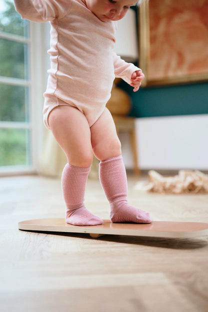 Baby mit rosefarbenen GoBabyGo Wollsocken auf Holzfussboden – sicherer Halt beim Laufenlernen