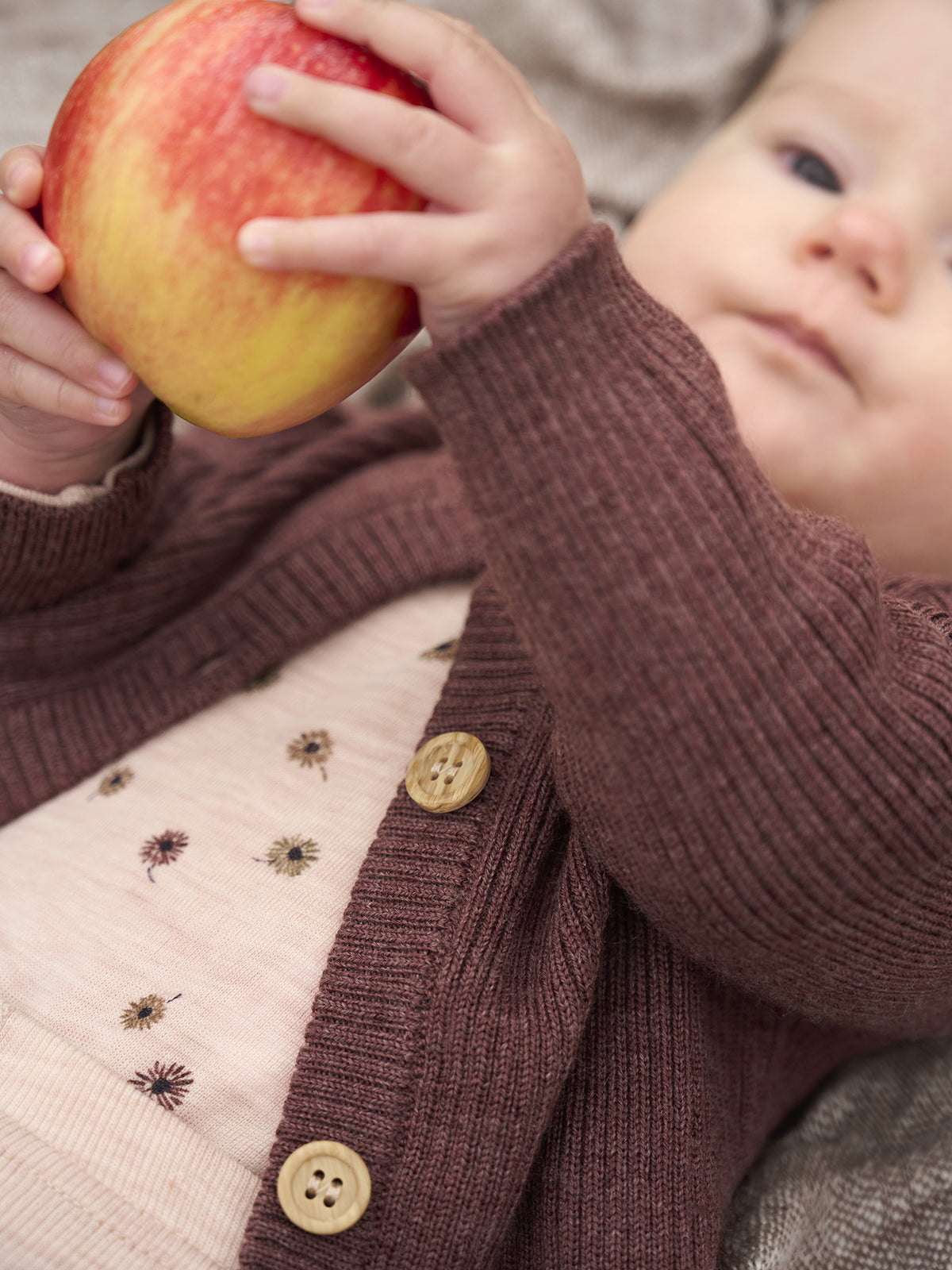 Baby trägt CeLaVi Wollbody mit Blumenmuster in Rosa unter Strickjacke – im Bärechind Winterthur, Zürich Schweiz.