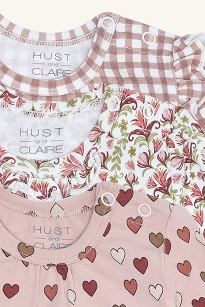 Detailaufnahme der Hust & Claire Babybodies mit Karomuster, floralem Print, Rüschen und Herzmuster in Rosatönen.