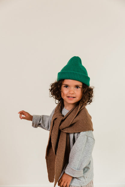 Kind trägt die grüne Merino Beanie von Hvid kombiniert mit einem braunen Strickschal