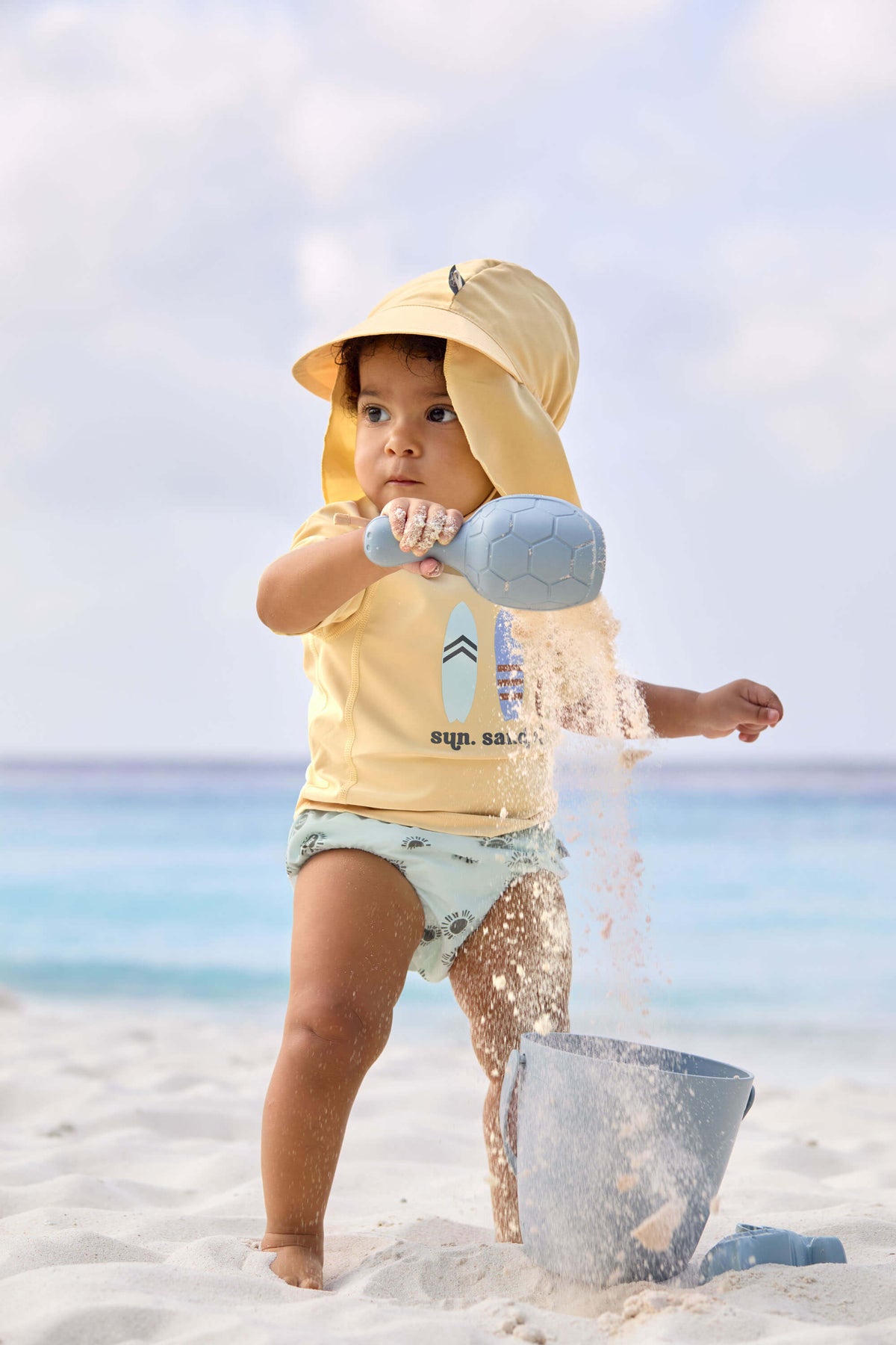Sonnenhut von Lässig für Babys in Gelb – mit UV-Schutz 80 & langem Nackenschutz, Angezogen an Strand.