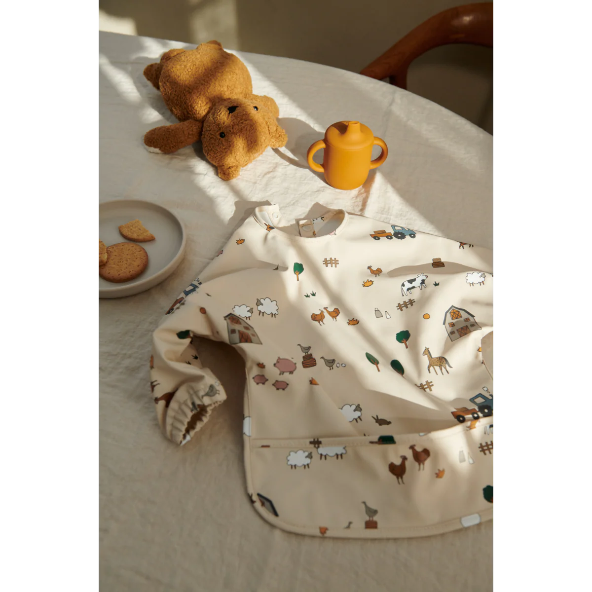 Kind trägt das Liewood Merle Langarm-Lätzchen mit Bauernhof-Print beim Essen am Tisch