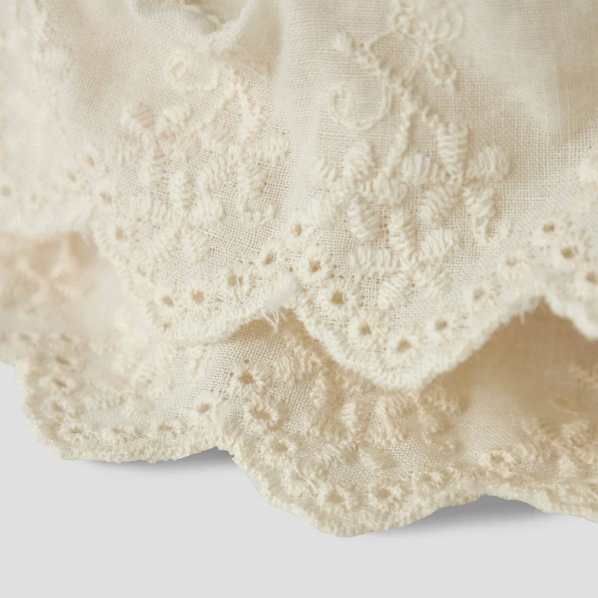 Detailaufnahme des cremefarbenen Lil' Atelier Frida Haargummis mit dekorativer Lochstickerei und gewelltem Stoffrand